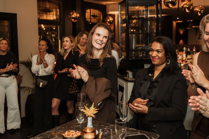 Een groep vrouwen lacht en klapt samen tijdens een She Society-avond