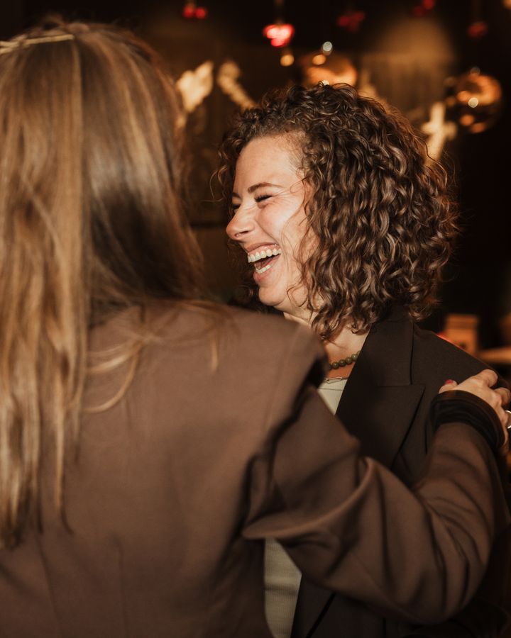 Twee vrouwen omhelzen elkaar lachend tijdens de She Society-kerstborrel