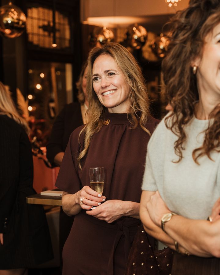 Een lachende gast met een glas champagne onder de kerstlichtjes